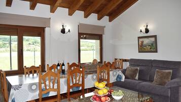 Un comedor con una mesa dispuesta para seis personas, rodeada de sillas de madera, una mesa de centro de vidrio con fruta, y un sofá gris.