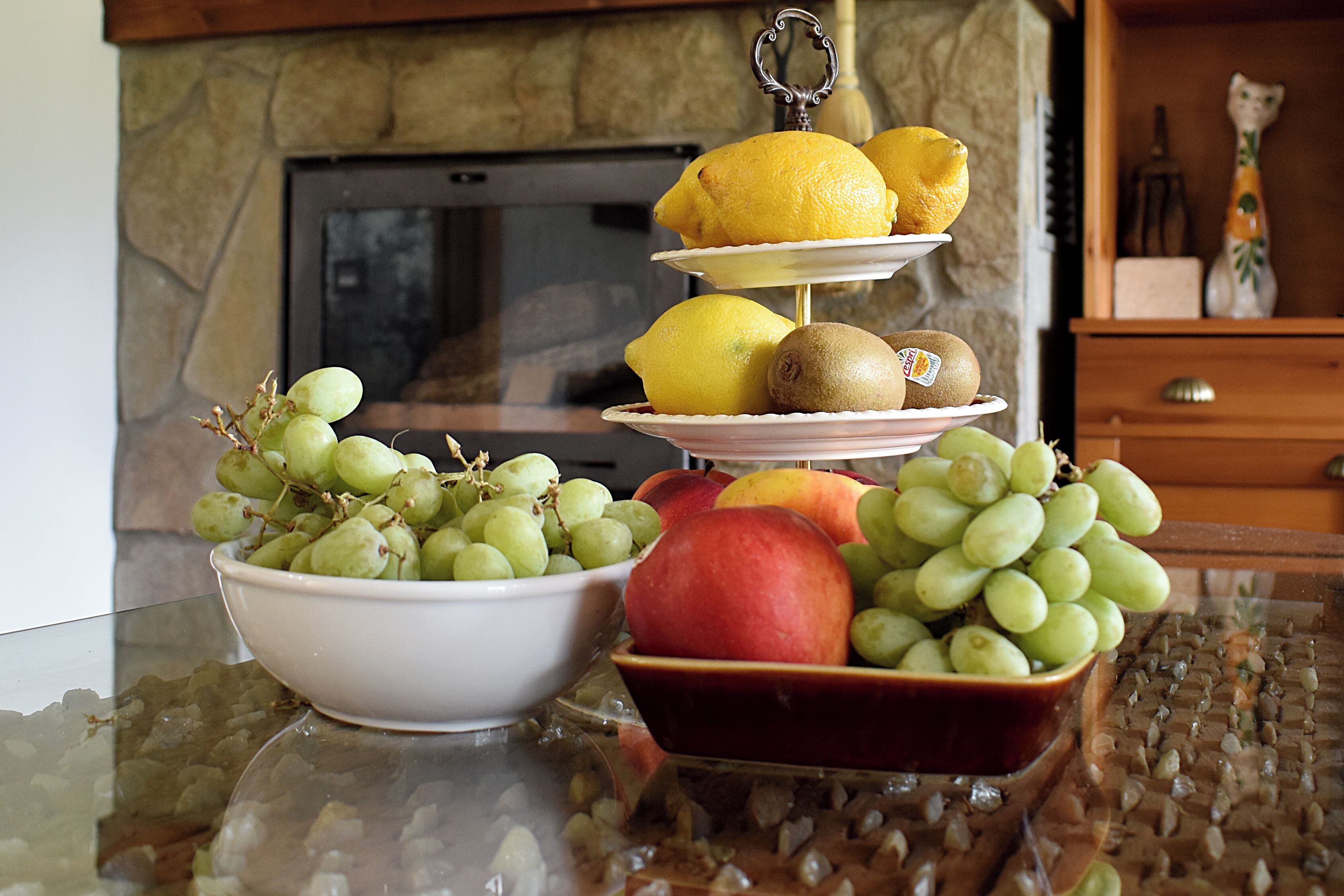 A fruit display with grapes, apples, and kiwis on a glass table.