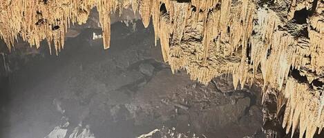 A cave interior with stalactites and stalagmites, dim lighting, and rugged rock formations.