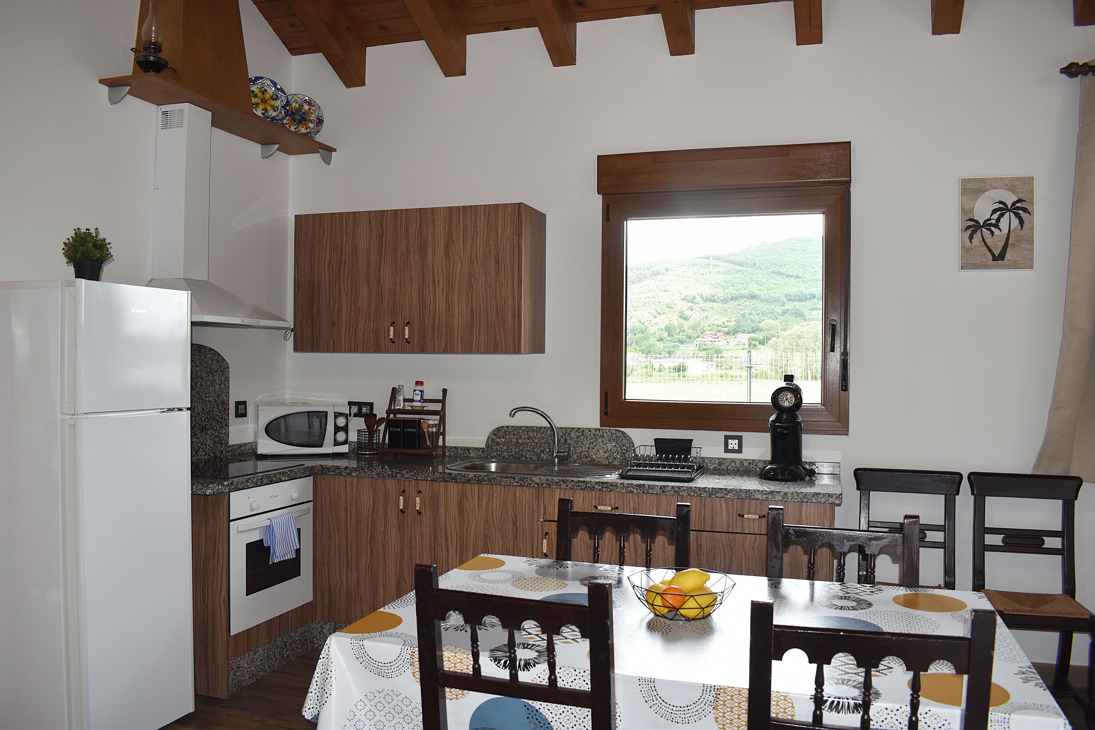 Una cocina con armarios de madera, un refrigerador blanco, un microondas y una mesa de comedor con sillas.