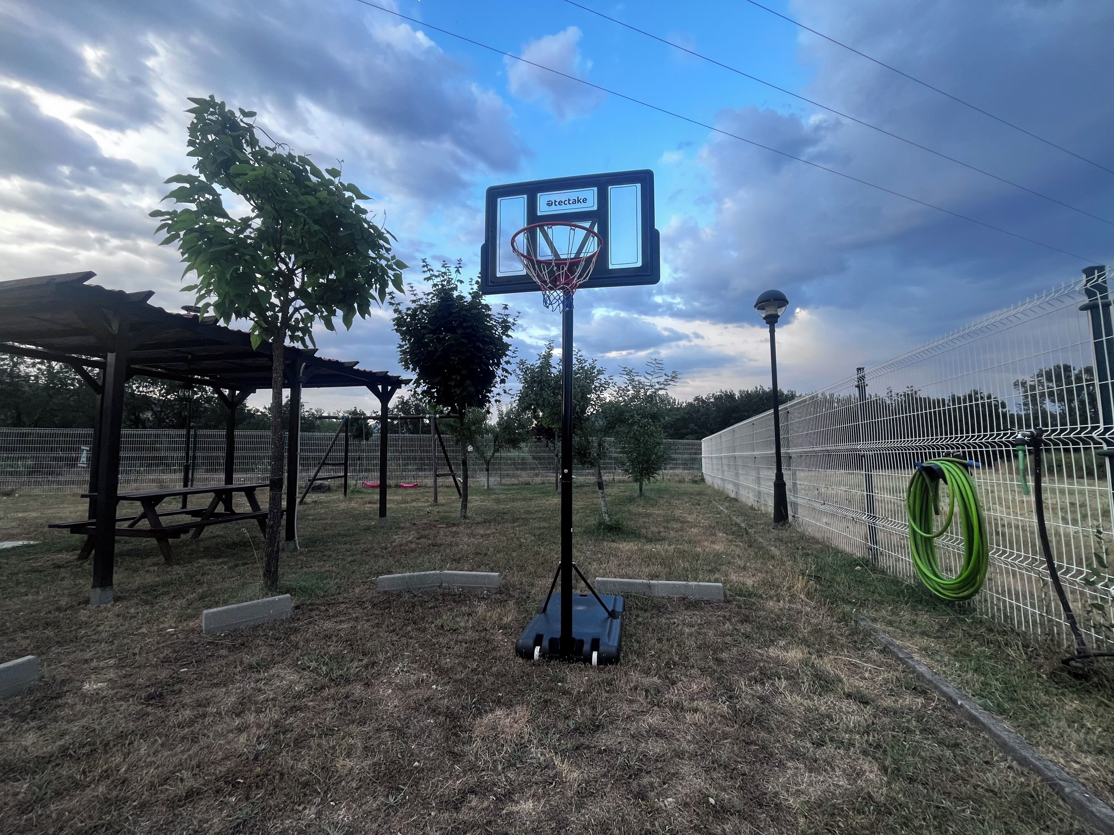Canasta de baloncesto en un área con césped, una mesa de picnic y una cerca.