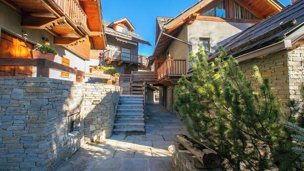 A narrow stone pathway leading to wooden buildings with balconies and a pine tree. - Fiori di Miele few Step From Skiing (Bardonecchia)