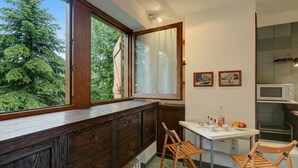 A kitchen with a window, wooden cabinets, a microwave, and a table with chairs. - Fiori di Miele few Step From Skiing (Bardonecchia)