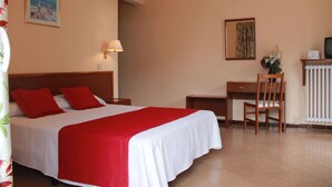 A hotel room with a bed, a desk, a chair, a lamp, and a radiator. - Terramar (Calella)