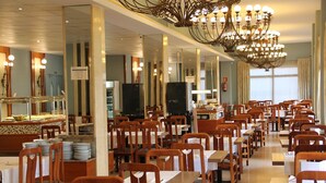 A spacious dining area with multiple tables and chairs, a central buffet, and a large chandelier. - Terramar (Calella)