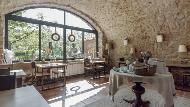 Un coin repas au style rustique, avec des murs en pierre, de grandes fenêtres et un assortiment de tables et de chaises.