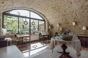Un comedor rústico con paredes de piedra, ventanas amplias y diferentes mesas y sillas.