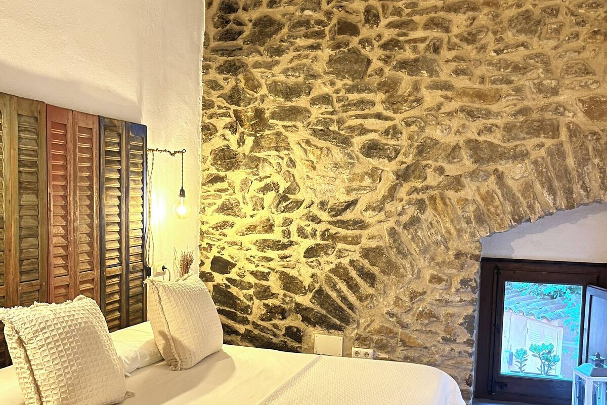 Een slaapkamer met een stenen muur, een bed met witte beddengoed en een houten vloer.