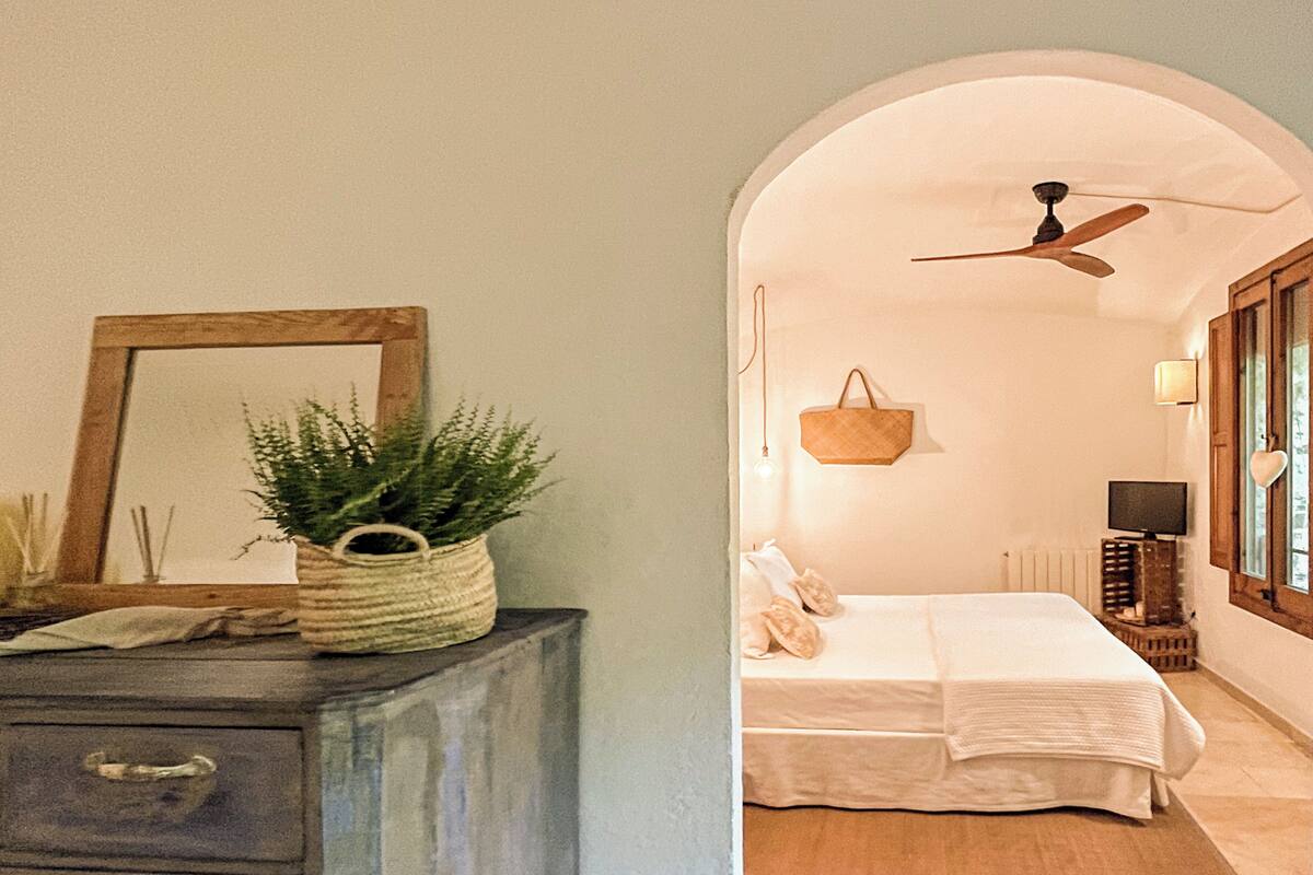Een slaapkamer met een bed, een plafondventilator, een nachtkastje, een lamp en een raam met gordijnen.