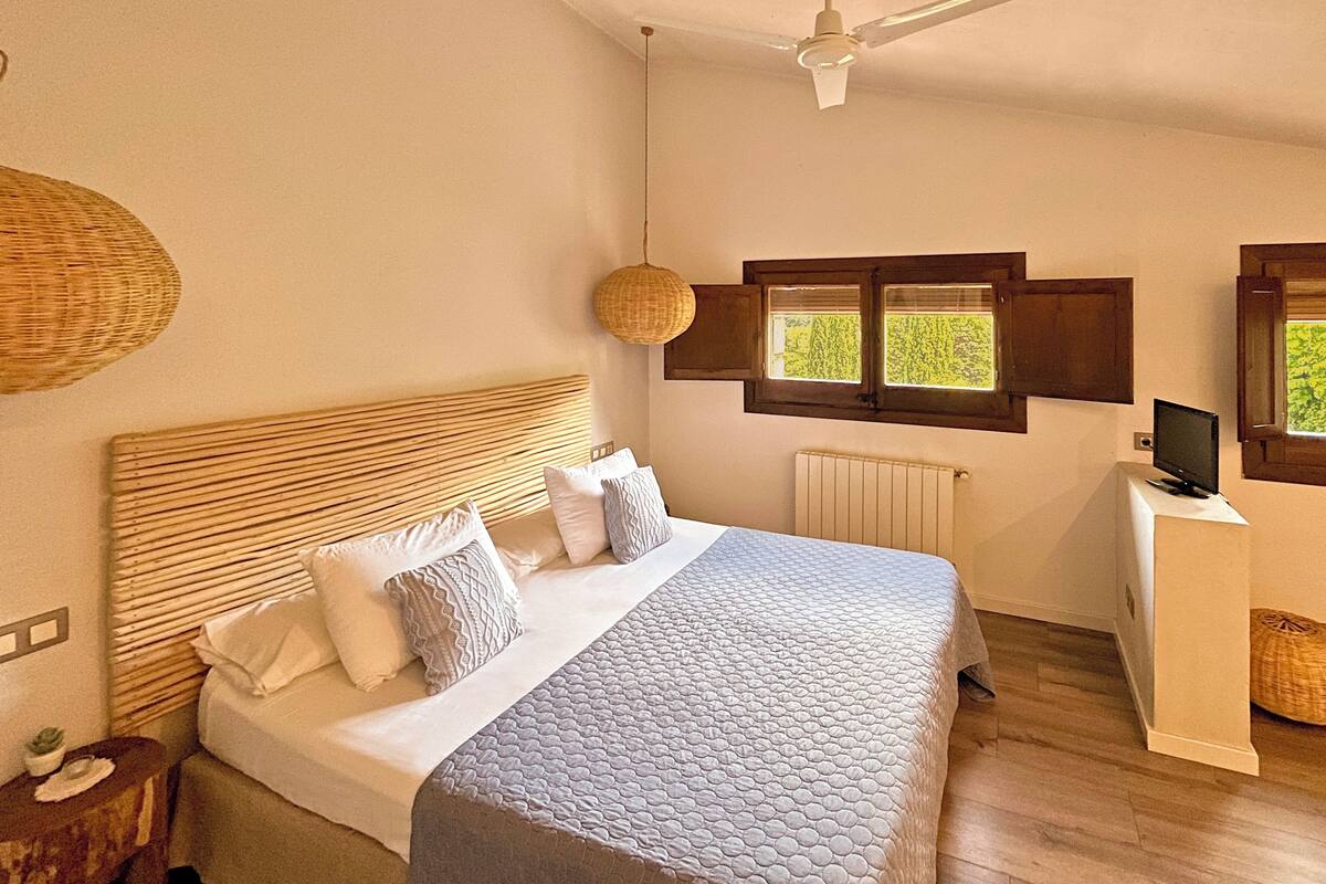 Een slaapkamer met een bed, een plafondventilator, een raam en een tv op een standaard.