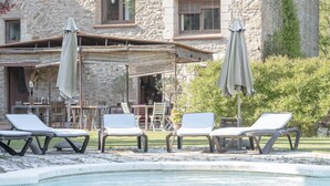 Un bâtiment en pierre doté d’un espace piscine comprenant des chaises longues et des parasols.