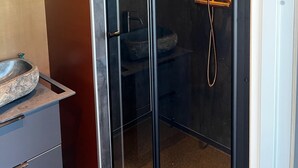 Un baño moderno con ducha envuelta en vidrio, tocador de madera y espejo grande.