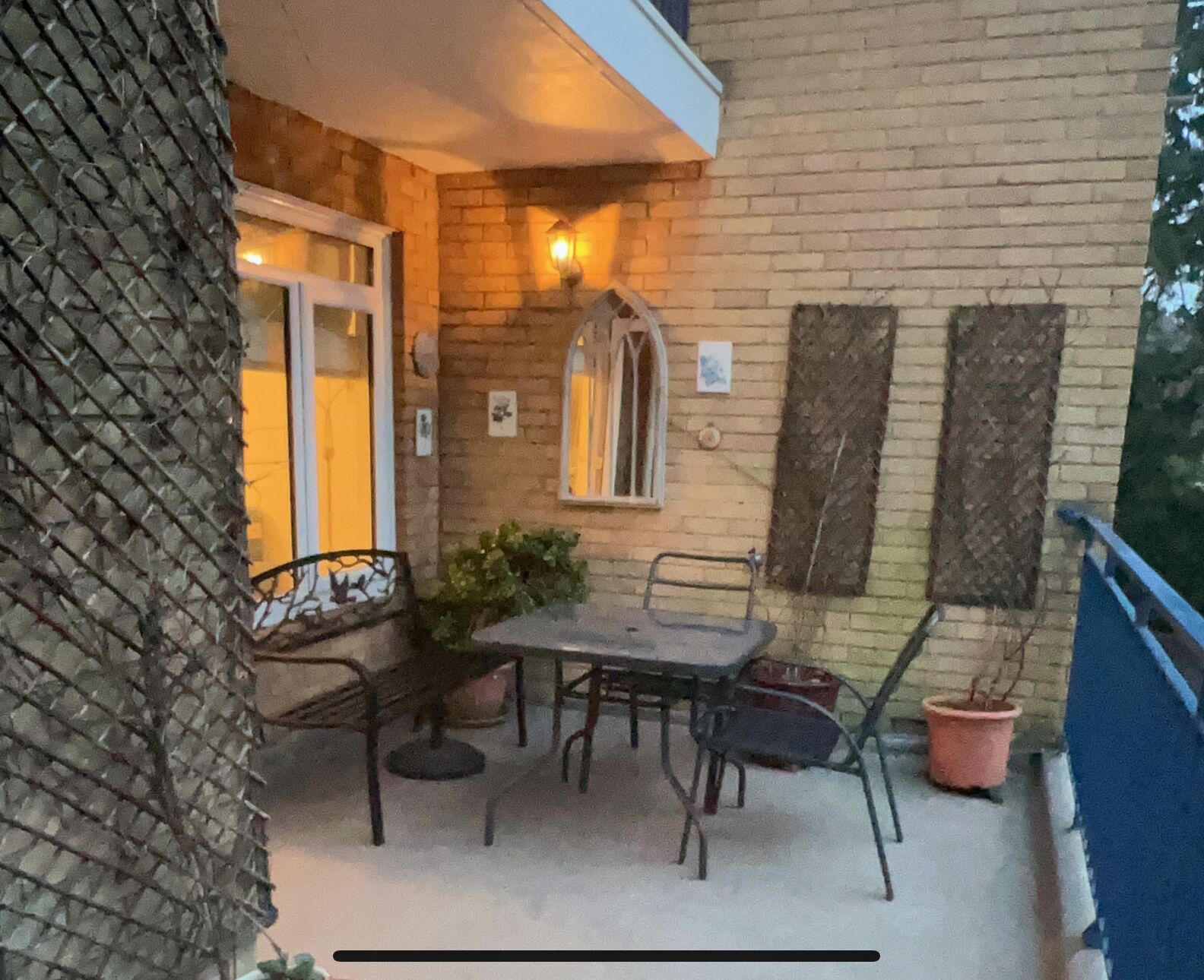 Un patio techado al aire libre con una mesa y sillas, una planta en maceta y un muro de ladrillo.