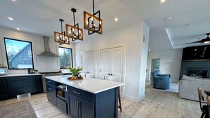 Une cuisine moderne dotée d’un grand îlot central, de meubles de rangement aux couleurs sombres et de luminaires suspendus.