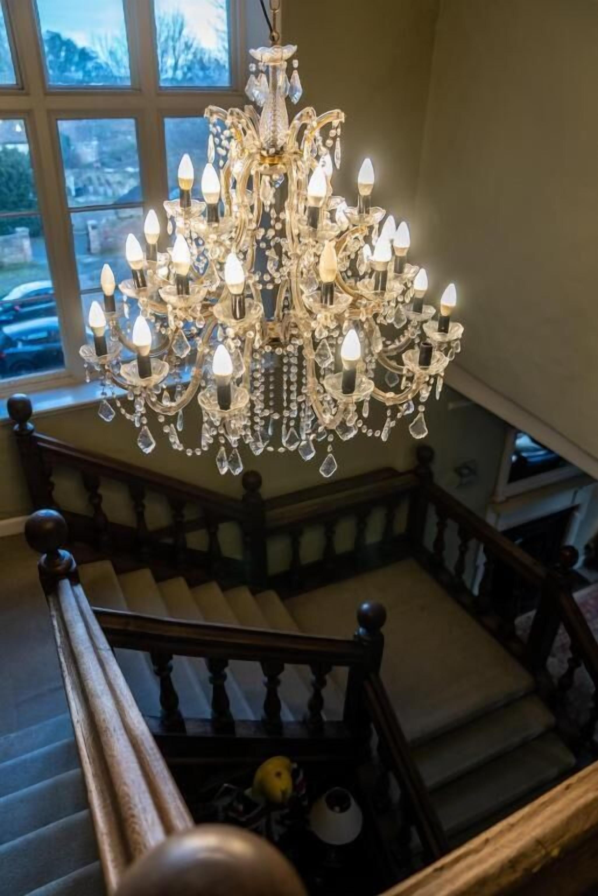 A grand chandelier with multiple lights hanging from a wooden staircase railing.