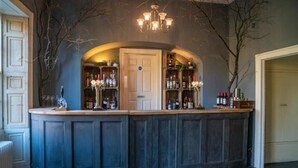 Zona de bar con mostrador de madera oscura, estantes con botellas y un candelabro.