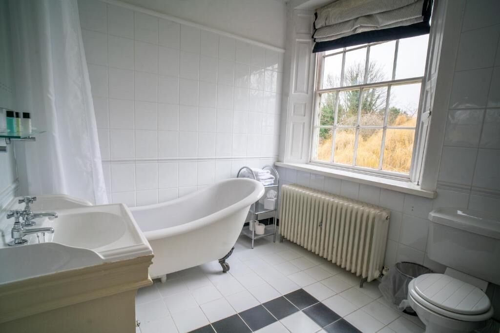 A bathroom with a freestanding bathtub, a toilet, a radiator, and a window with a view of the outdoors.