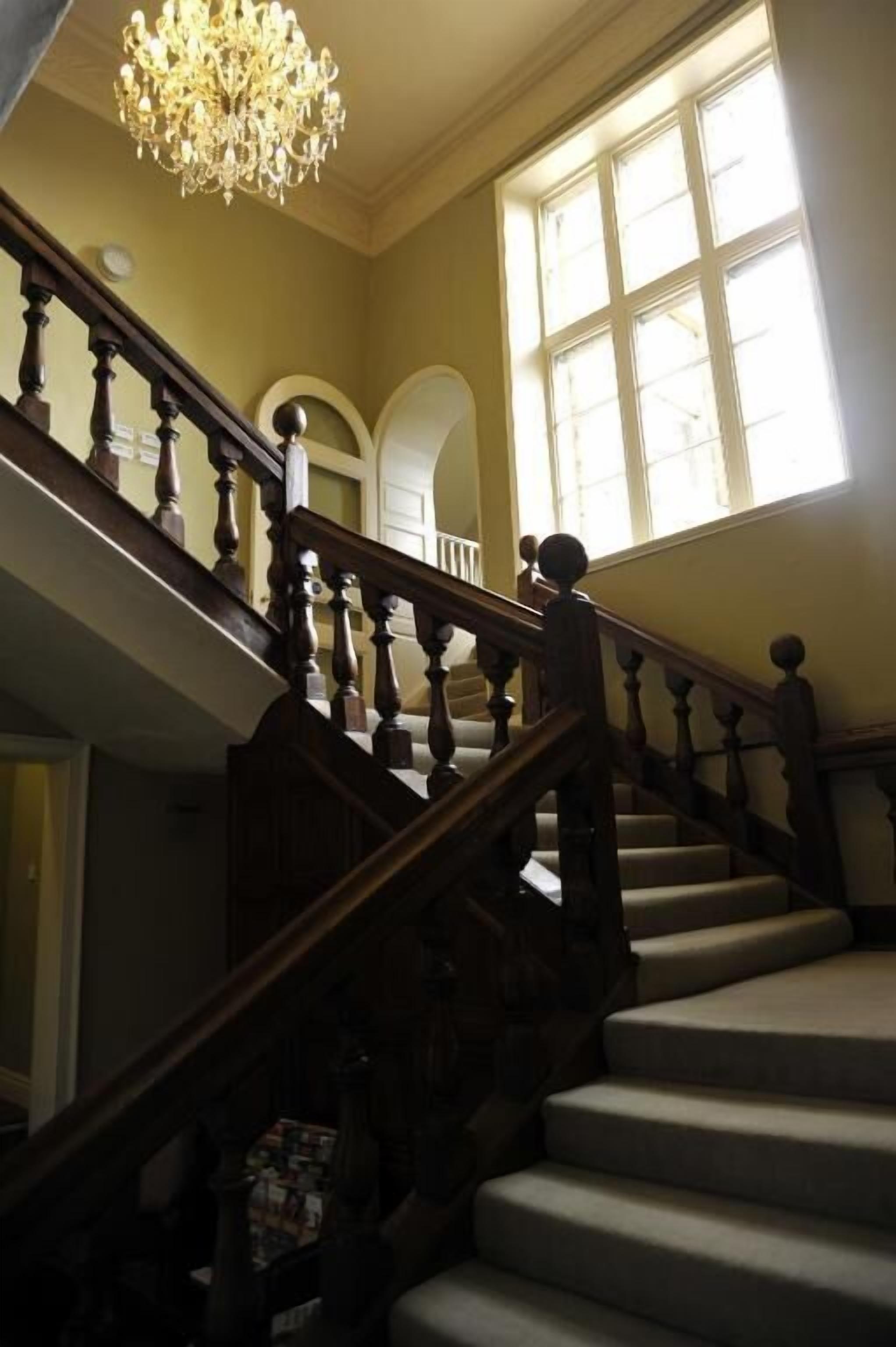 A grand staircase with a chandelier, leading to a landing with large windows.