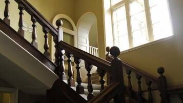 A grand staircase with a chandelier, leading to a landing with large windows.