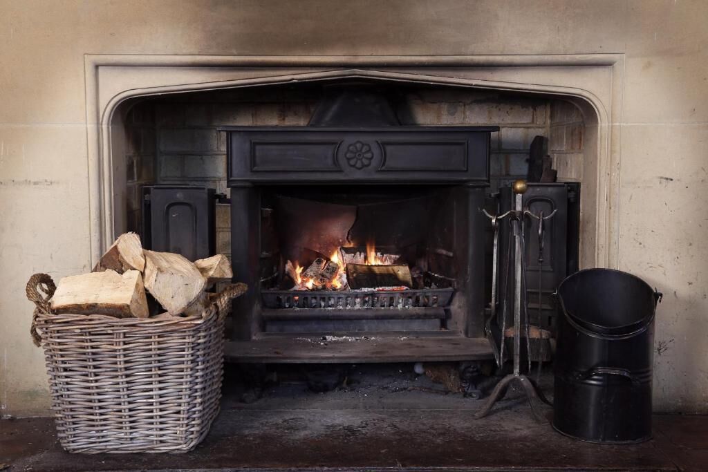 A fireplace with logs, a basket of firewood, and a bucket.