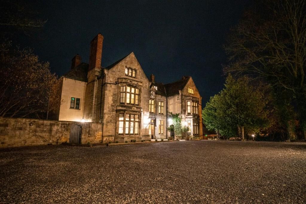 A large stone building with multiple windows and a gravel driveway at night.