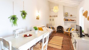 A cozy living room with a white sofa, a dining table with a bowl of fruit, and a fireplace. - Cortijo Horizonte Solset (Frigiliana)