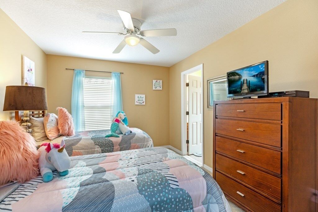 A bedroom with two beds, a ceiling fan, a dresser, a television, and a window with blinds.