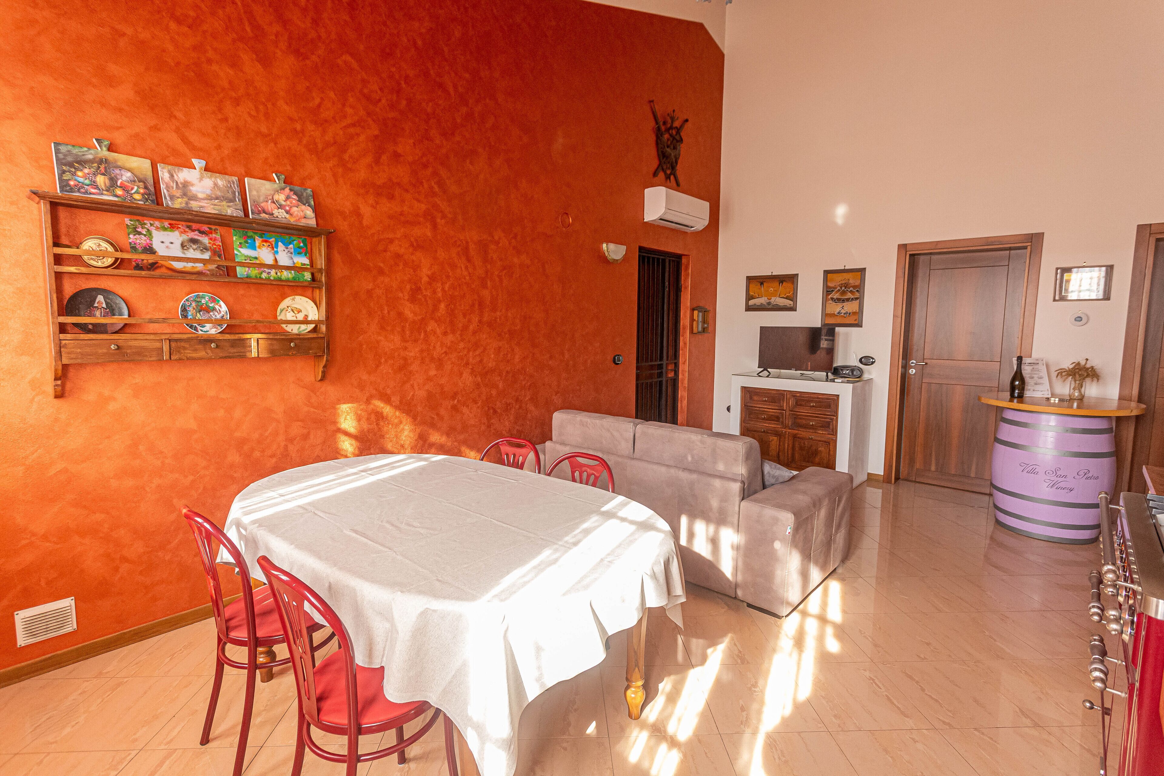 A dining area with a table and chairs, a sofa, and a shelf with plates and a clock.