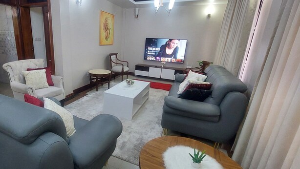 Una sala de estar moderna con sofás grises, una mesa de centro blanca y un televisor en la pared.