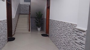 Un pasillo con suelo de baldosas, una escalera con pared texturizada y una planta en maceta.