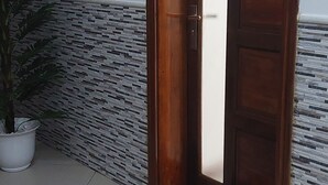 Una puerta de madera con un número, una planta en maceta y un suelo de baldosas.