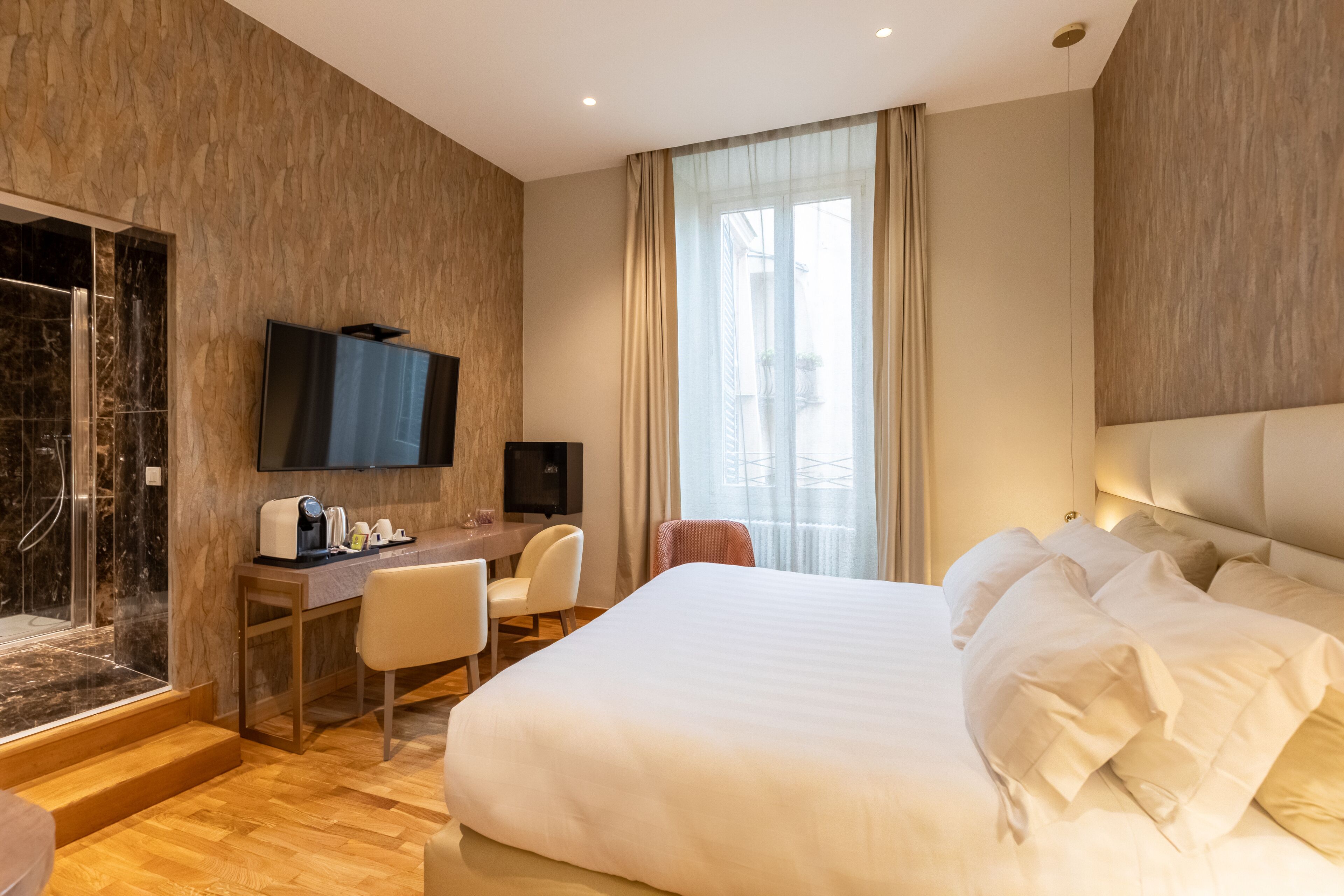 Une chambre d’hôtel avec un grand lit, un bureau avec une chaise, une télévision et une salle de bain avec une douche en verre.