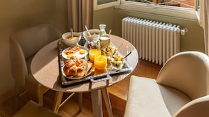 Taula de l'esmorzar amb croissants, suc d'aranja i cereals, situada en una habitació amb vista a edificis i vegetació a través d'una finestra.