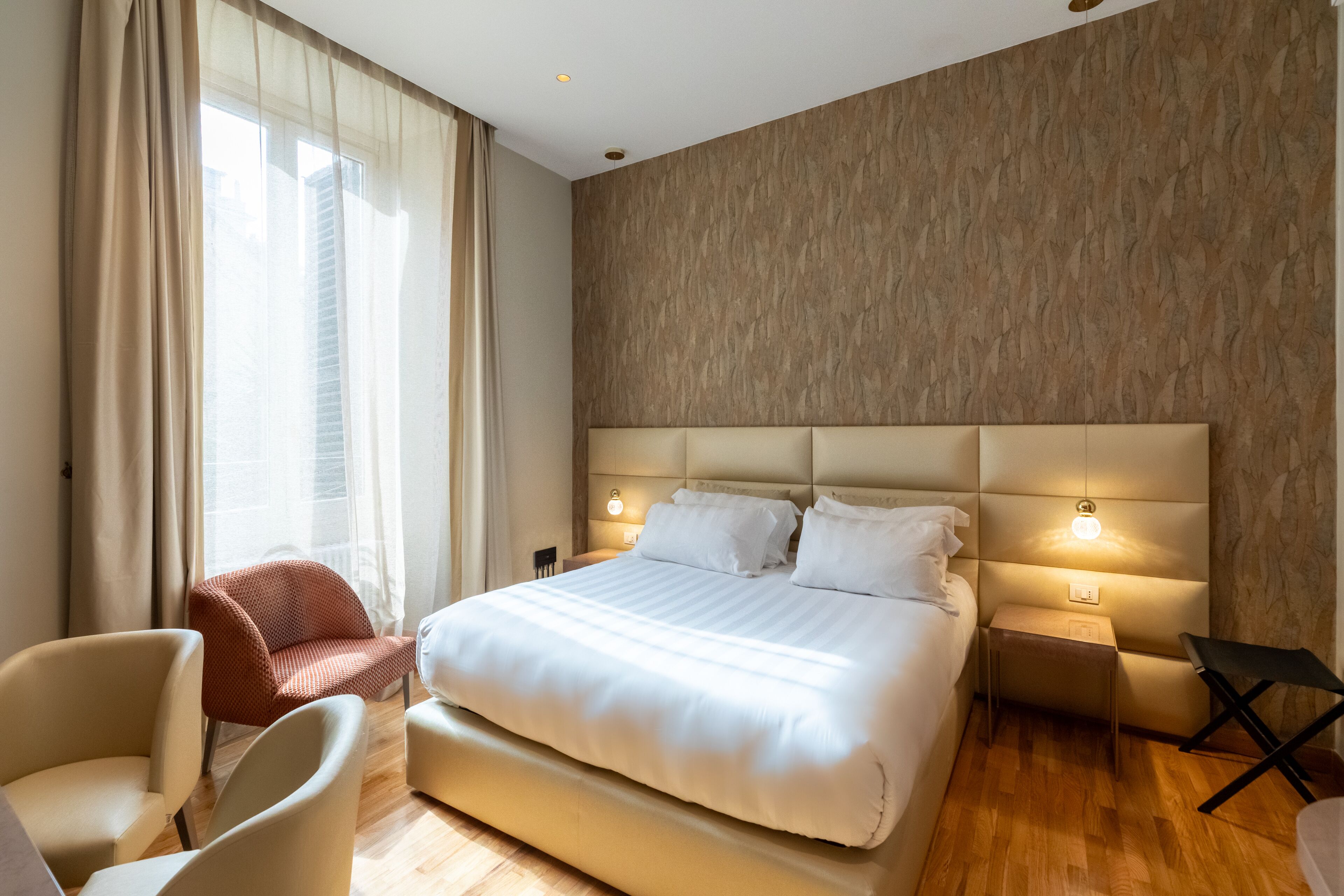 Une chambre d’hôtel moderne dotée d’un grand lit, de deux tables de chevet avec des lampes, d’un fauteuil et offrant une vue sur l’extérieur.