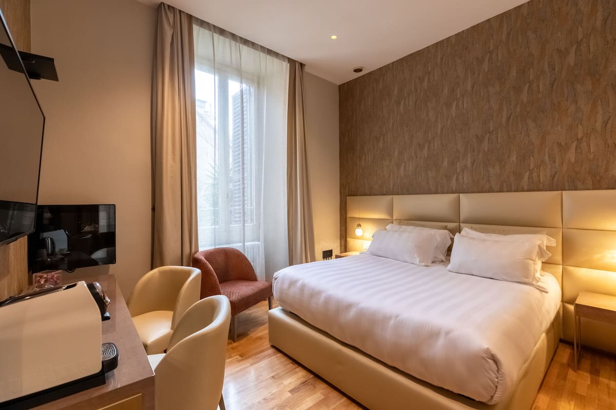 A hotel room with a large bed, a desk with a chair, a television, and a window with curtains.