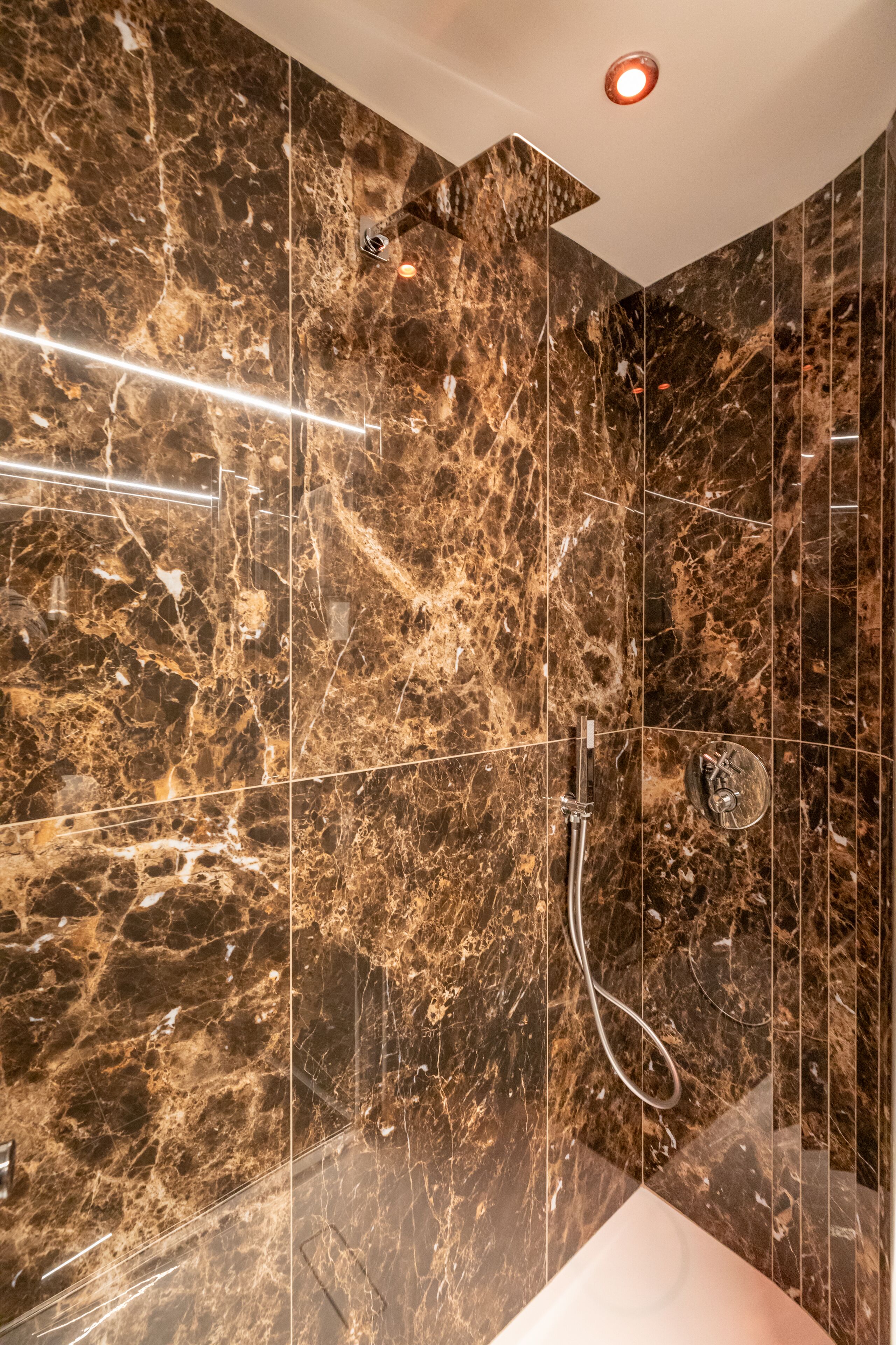 A modern bathroom with a marble wall and a glass-enclosed shower area.