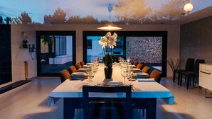 A modern dining room with a long table set for a meal, featuring a vase of flowers, and a view of the outdoors through large windows. - FOZ DO NEIVA 16 - Luxury stay in Foz do Neiva, Esposende, Portugal (Guilheta)