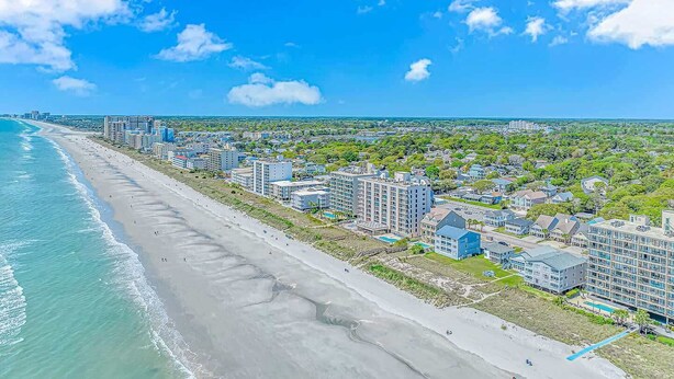 Zona hotelera frente al mar con propiedades en primera línea de playa, una playa de arena y un cielo azul despejado.