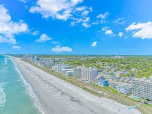 Zona hotelera frente al mar con propiedades en primera línea de playa, una playa de arena y un cielo azul despejado.