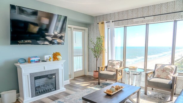 A living room with a fireplace, a television, and a view of the ocean.
