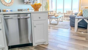 A modern kitchen with a dishwasher, a dining area with a table and chairs, and a large window offering a view.