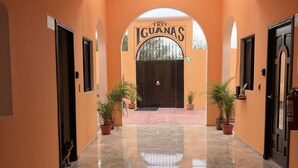 Un pasillo con suelo de baldosas que conduce a una verja negra con la inscripción 'Tres Iguanas'. Hay plantas en macetas a ambos lados del pasillo.