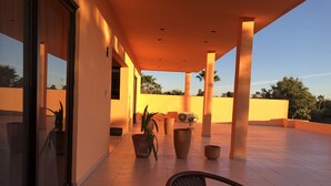 Un espacio al aire libre techado con suelo de baldosas, plantas en macetas y una silla.