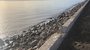 Una costa rocosa con un muro de concreto y una vista despejada del agua y montañas distantes.