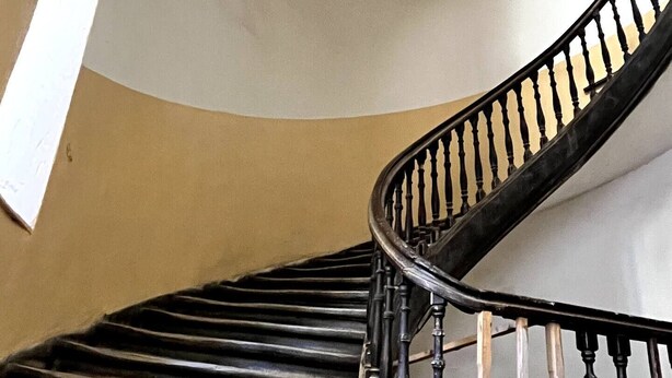 Uma escadaria em espiral com balaústres pretos e parede bege.
