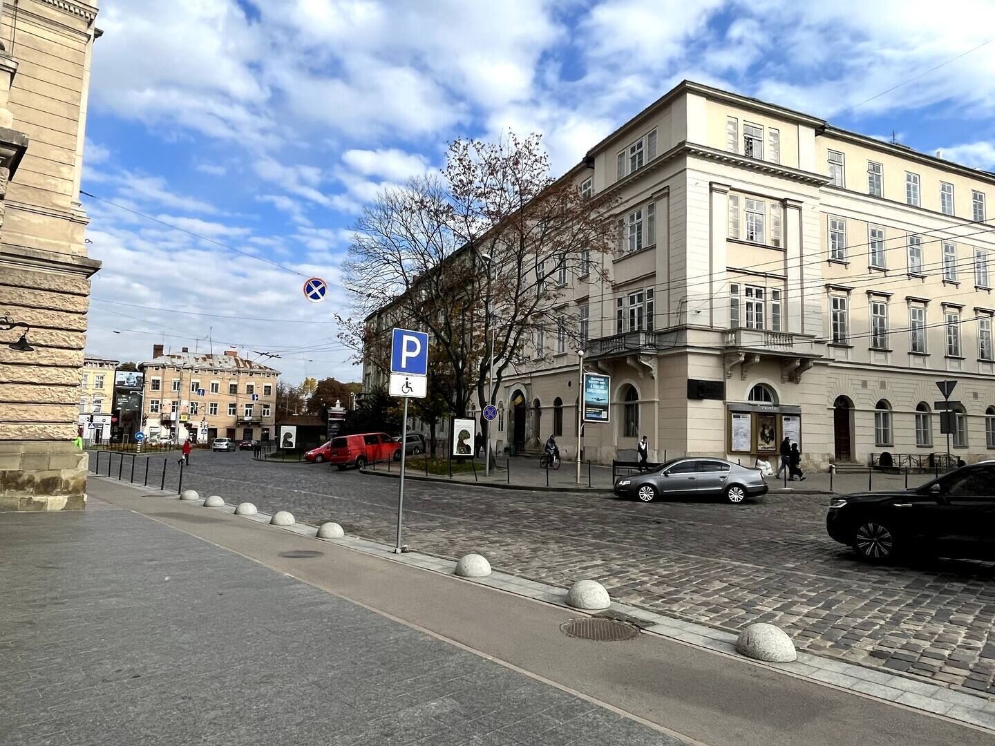 Een straat met een parkeersbord, een gebouw met klassieke architectuur en paaltjes langs het trottoir.