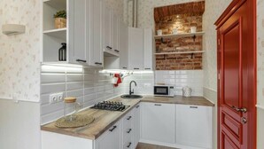 Uma cozinha compacta com armários brancos, bancada de madeira, fogão a gás, micro-ondas e uma porta vermelha.
