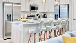 Cozinha moderna com eletrodomésticos de aço inoxidável, uma ilha central com banquetas e iluminação pendente.