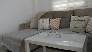 Ein Wohnzimmer mit einem beigen Sofa, gemusterten Kissen, einem weißen Couchtisch und einem gerahmten Bild an der Wand.