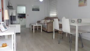 Ein modernes Wohnzimmer mit Sofa, Esstisch und Stühlen. Im Hintergrund ist eine Küche zu sehen.